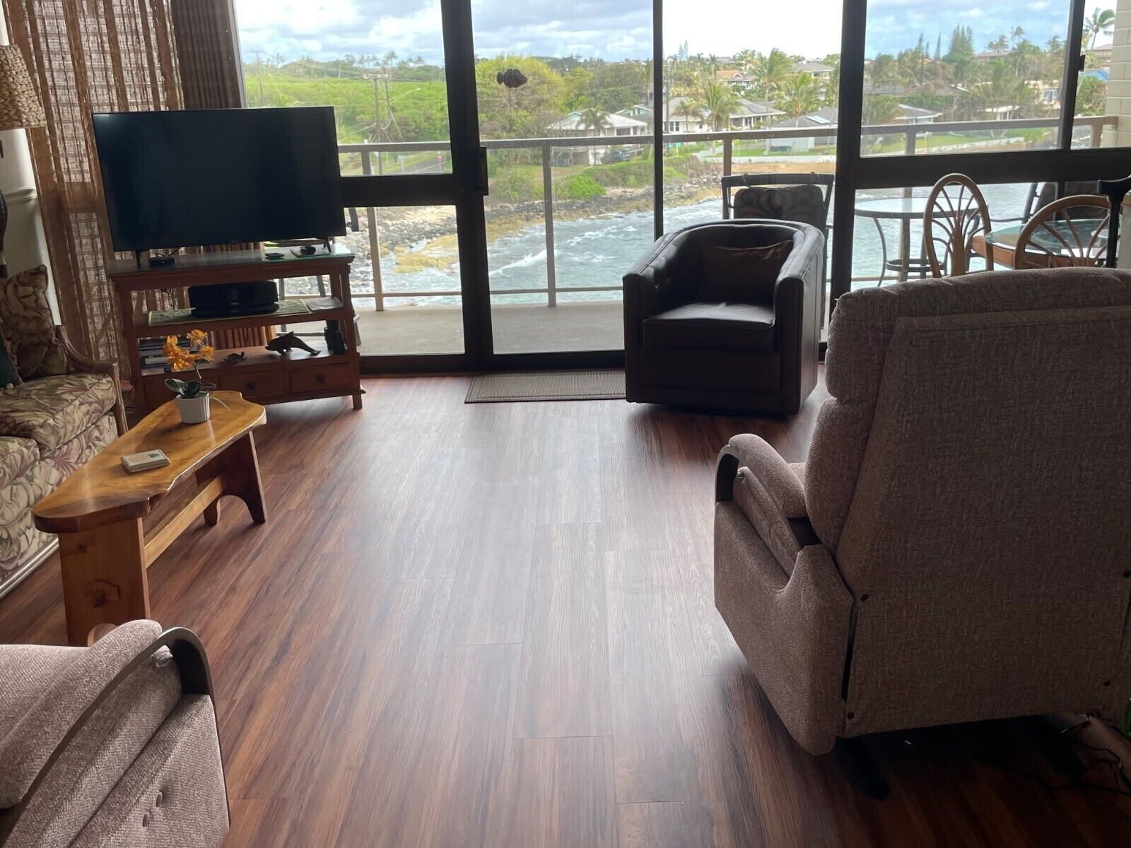 A living room with a television, a sofa, a chair, and a view of the ocean.