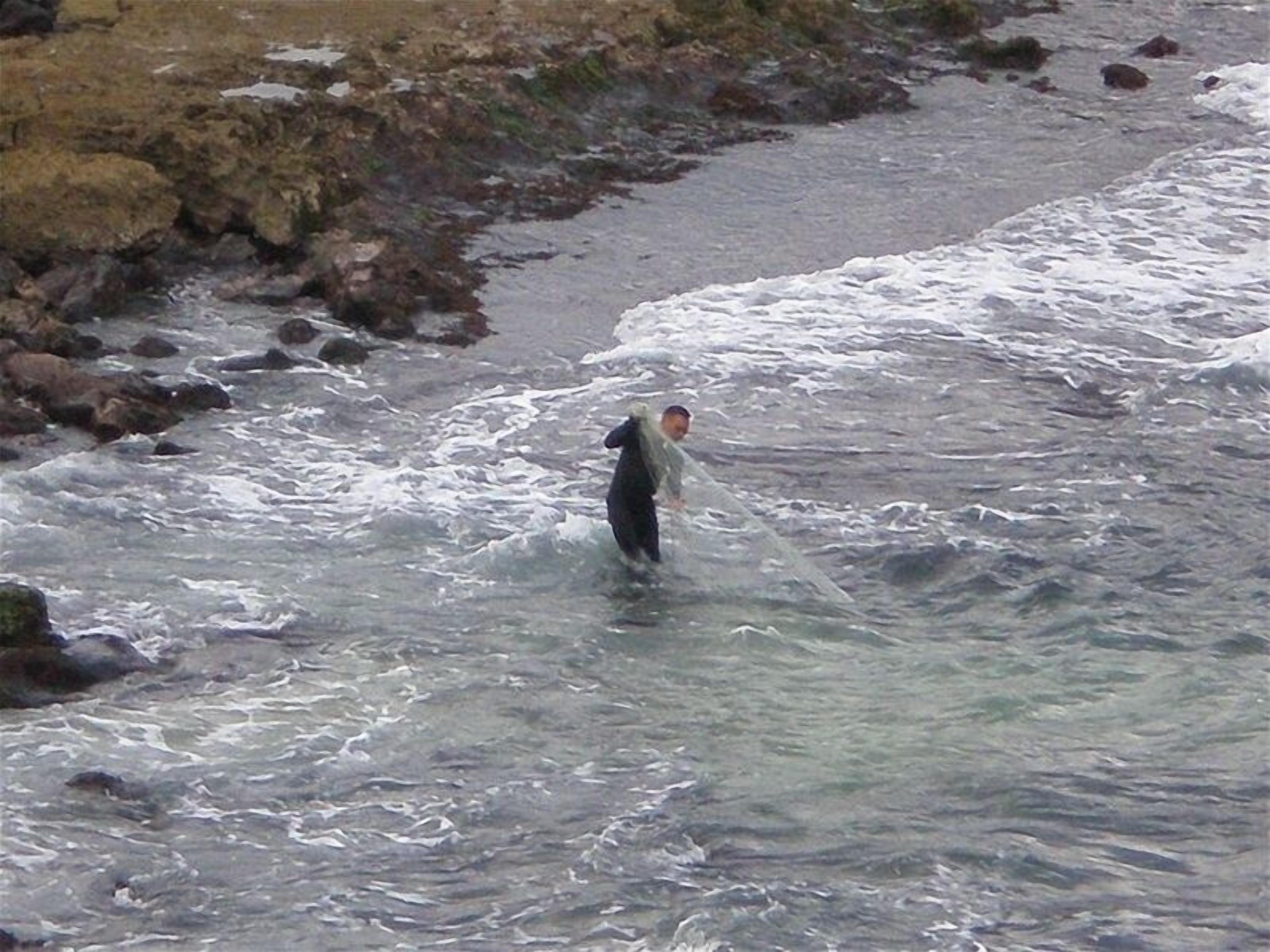 A person wading through a river with rocks and waves.