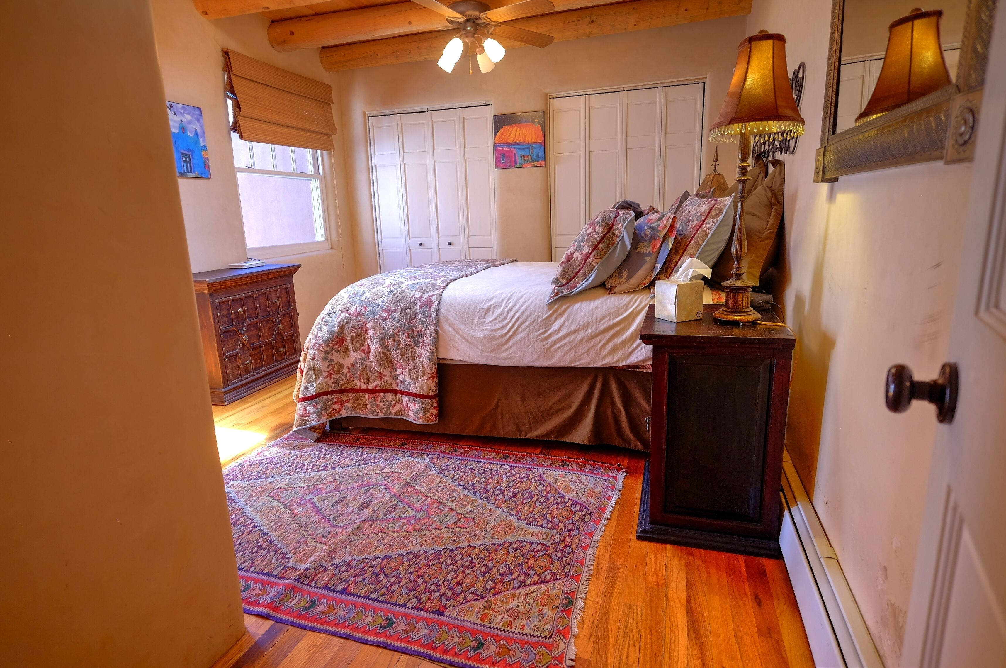 A bedroom with a bed, a wooden dresser, a patterned rug, and a ceiling fan.