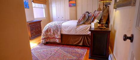 A bedroom with a bed, a wooden dresser, a patterned rug, and a ceiling fan.