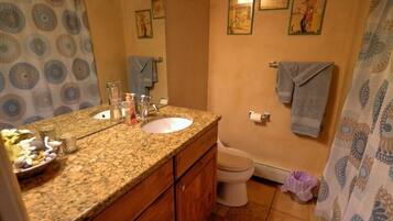A bathroom with a granite countertop sink, two mirrors, a toilet, and a shower curtain.