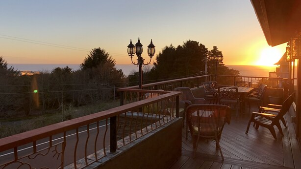 A wooden deck with outdoor furniture and a railing, overlooking a sunset over the ocean. - Majestic View, Luxury Home, Corp Retreat, Sauna, Roads End (Lincoln City)