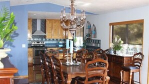 A dining area with a wooden table and chairs, a chandelier, and a view of the kitchen in the background. - Majestic View, Luxury Home, Corp Retreat, Sauna, Roads End (Lincoln City)