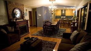 A living room with a fireplace, a dining area with a chandelier, and a kitchen in the background. - Majestic View, Luxury Home, Corp Retreat, Sauna, Roads End (Lincoln City)