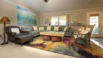 Ein Wohnzimmer mit einem großen Wandbild einer Welle, einer Couch, einem Couchtisch und zwei Sesseln.