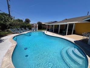 A swimming pool with a curved edge, surrounded by lounge chairs and a covered patio area.