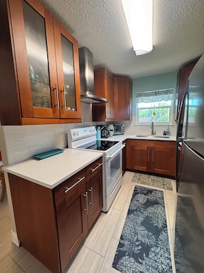 A kitchen with wooden cabinets, a stove, a refrigerator, and a window with a view of greenery.