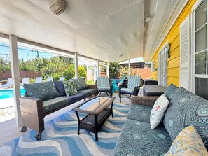 A covered patio with a pool, outdoor furniture, and a yellow building in the background.