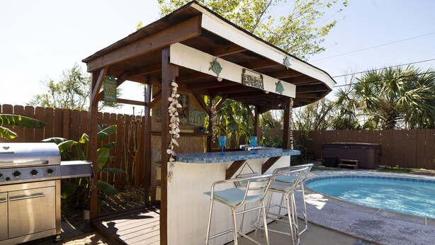 Ein überdachter Außenbereich mit Bar, Pool, Barhocker und Grill.