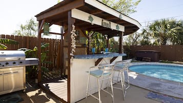 Ein überdachter Außenbereich mit Bar, Pool, Barhocker und Grill.