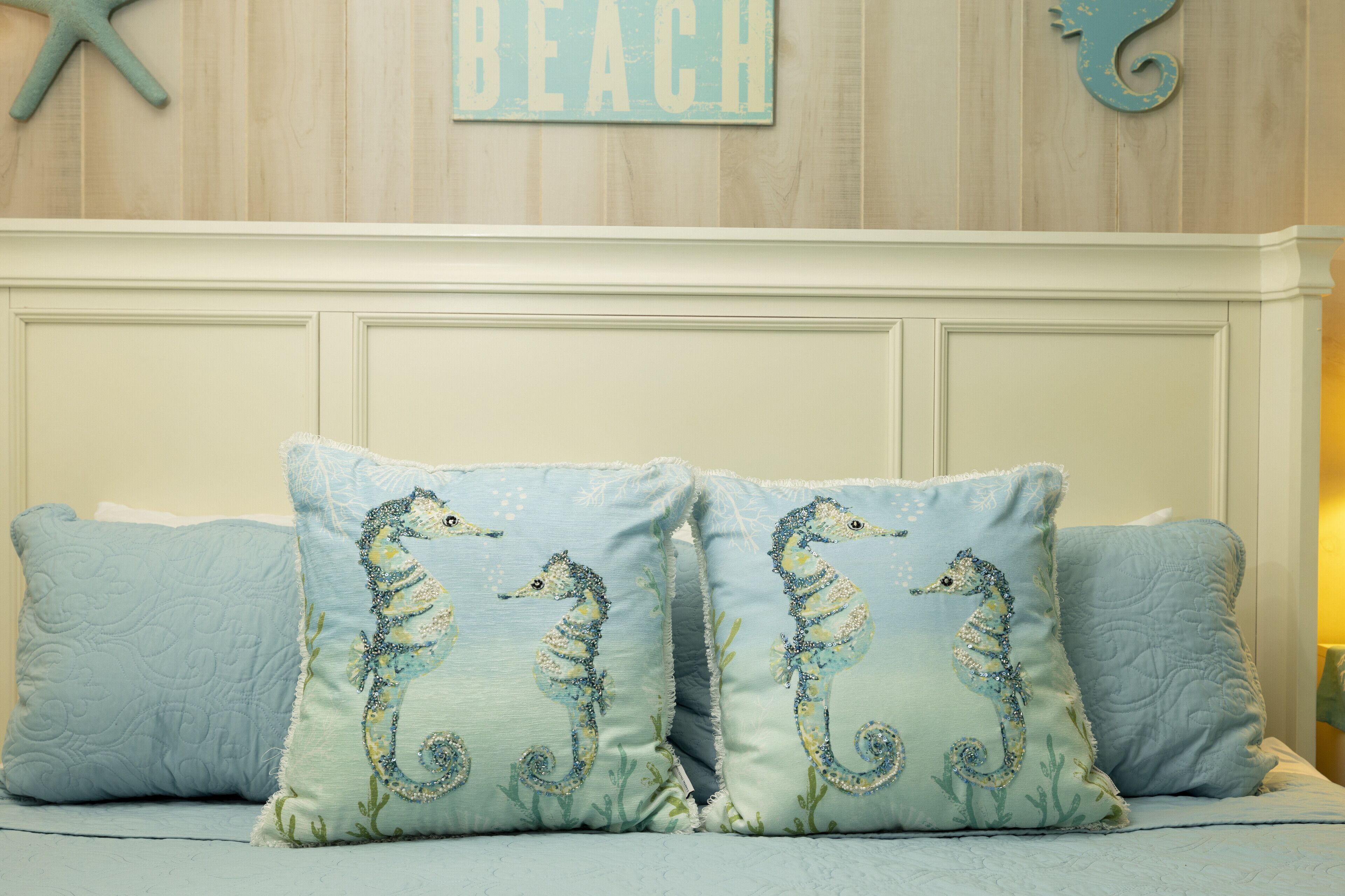Ein Schlafzimmer mit einem Bett, zwei Kissen mit Seepferdchen-Motiven, einer Wand mit dem Schriftzug "BEACH" und einer Meerstern-Dekoration.