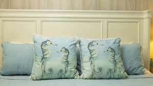 Ein Schlafzimmer mit einem Bett, zwei Kissen mit Seepferdchen-Motiven, einer Wand mit dem Schriftzug "BEACH" und einer Meerstern-Dekoration.