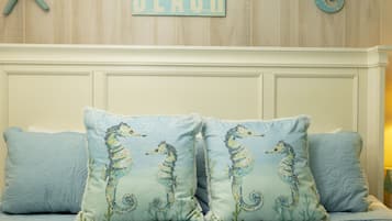 Ein Schlafzimmer mit einem Bett, zwei Kissen mit Seepferdchen-Motiven, einer Wand mit dem Schriftzug "BEACH" und einer Meerstern-Dekoration.
