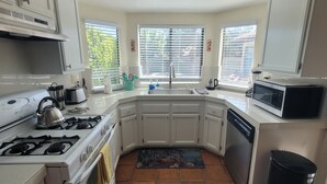 A compact kitchen with white cabinets, a gas stove, a microwave, and a sink.