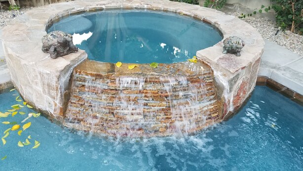 A stone fountain with water flowing into a pool, surrounded by a stone border and decorative statues.