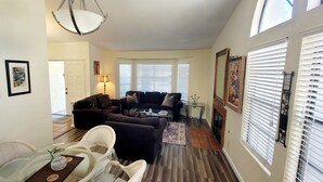 A cozy living room with a dark-colored sofa, a coffee table, and a lamp. There are framed pictures on the wall and a door leading to another room.