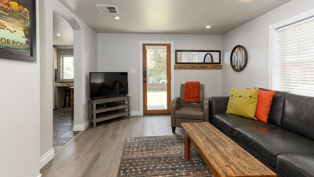 A living room with a television, a sofa, a coffee table, and a door leading to an outdoor area. - Westside Cottage │Fenced Yards │Hot Tub │One Block to Galveston │Guest Favorite (Bend)
