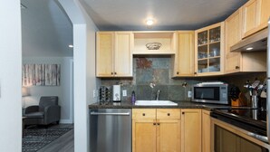 A modern kitchen with wooden cabinets, stainless steel appliances, and a tiled backsplash. - Westside Cottage │Fenced Yards │Hot Tub │One Block to Galveston │Guest Favorite (Bend)