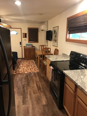 A compact kitchen with a refrigerator, stove, and wooden cabinets. - Cottage-Very Close to Beach-Quiet A/C-Full Kitchen with Range/Oven-Deck-Laundry (Hauula)