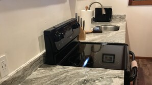 A kitchen with a black stove, a sink, and a marble countertop.