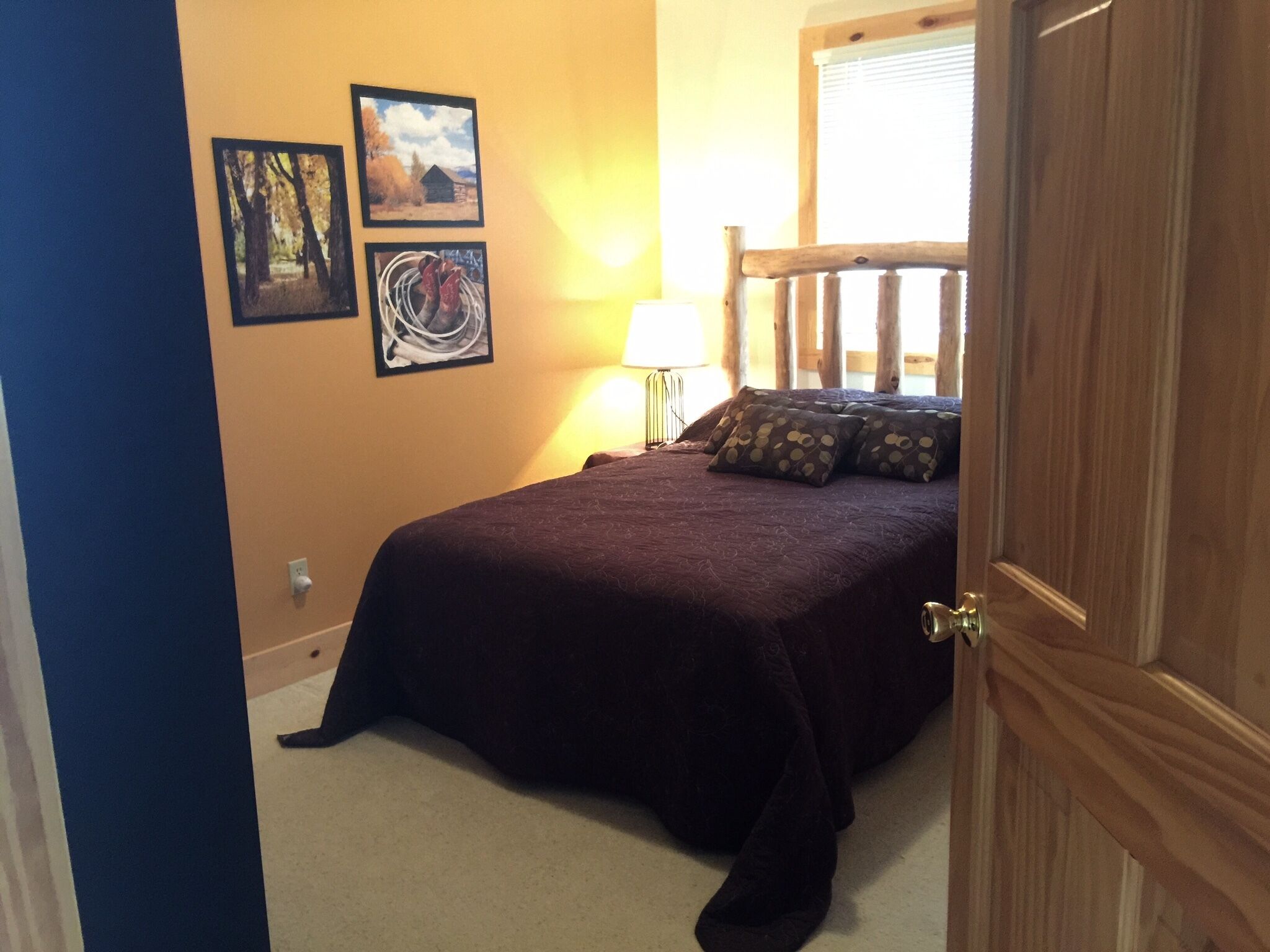 A bedroom with a bed, a nightstand, and a window. There are three framed pictures on the wall.