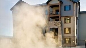 Una piscina de hidromasaje con vapor saliendo del agua, rodeada por un edificio con varios balcones y ventanas.