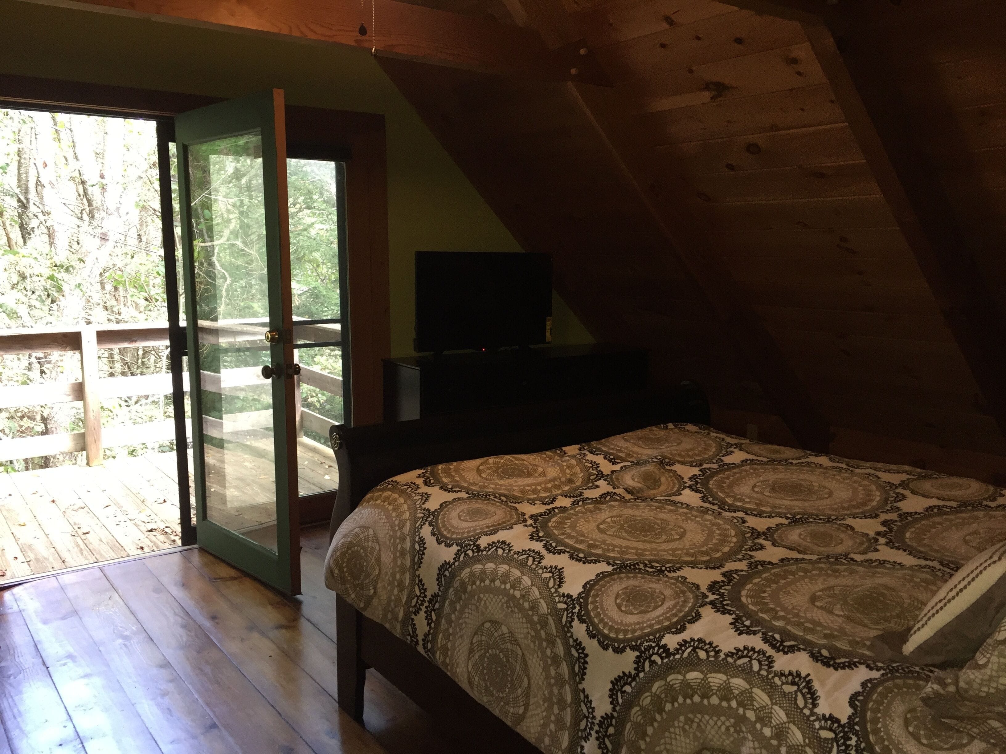Une chambre dotée d’un grand lit, d’un téléviseur posé sur un meuble et d’une porte-fenêtre coulissante donnant sur une terrasse extérieure.