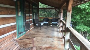 Un porche de madera con sillas de mimbre y un banco, con vista a una zona boscosa.
