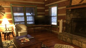 Una sala de estar acogedora con paredes de madera, chimenea, televisor, un sillón estampado y una mesa de centro.