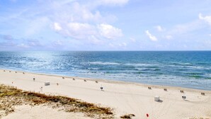 Ein Strand mit blauem Himmel, ruhigem Meer und mehreren Liegestühlen am Ufer.