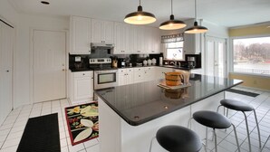 A modern kitchen with white cabinets, a central island with bar stools, pendant lighting, and a view of a lake through the window. - family vacation, BOATING, with heated pool Waterfront Lake wylie home -hot tub  (Charlotte)