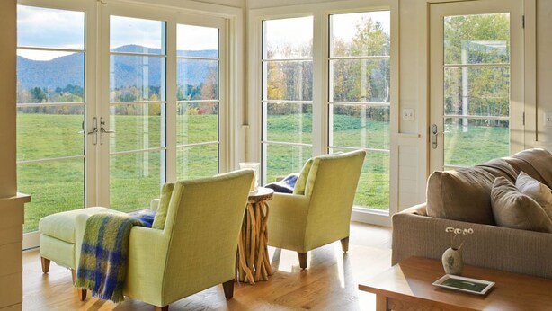 A spacious room with large windows, wooden beams, and a cozy seating area with chairs and a sofa. - Modern Farmhouse on 25 Acres / Superb Views. (Rochester)