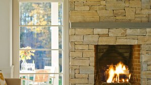 A cozy living room with a stone fireplace, a large window, and a dining area with outdoor seating. - Modern Farmhouse on 25 Acres / Superb Views. (Rochester)
