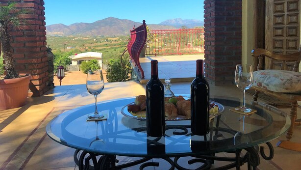 Une table en verre avec des bouteilles de vin et des verres, une assiette de nourriture et une vue sur les montagnes.