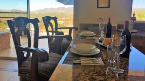 Une table à manger dressée avec des assiettes, des verres et des bouteilles, donnant sur un paysage montagneux.