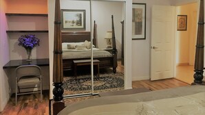 Une chambre à coucher avec un lit à baldaquin, un bureau avec une chaise, un vase de fleurs et une porte donnant sur une autre pièce.