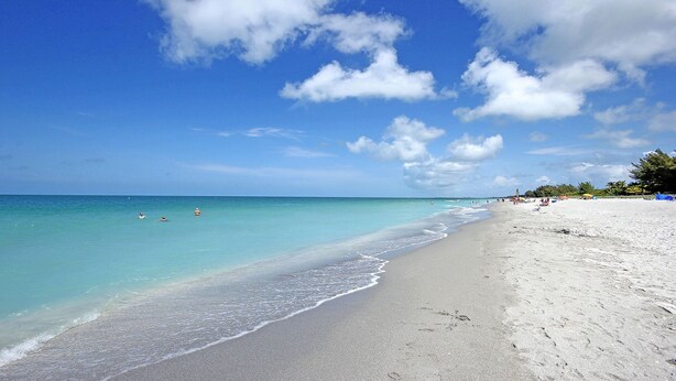 A beach with clear turquoise water, white sand, and a few people swimming. - Fantastic Island Getaway at Sunset Captiva 48 (Captiva)