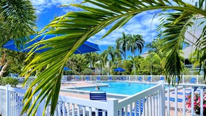 A pool area with a white fence, blue umbrellas, and lounge chairs. - Fantastic Island Getaway at Sunset Captiva 48 (Captiva)