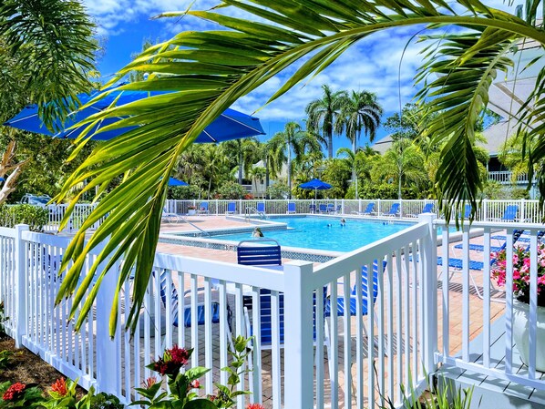 A pool area with a white fence, blue umbrellas, and lounge chairs. - Fantastic Island Getaway at Sunset Captiva 48 (Captiva)