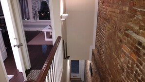Eine Treppe mit hölzernem Geländer und weißen Spindeln, die zu einem Raum mit Backsteinwand und einem fenster mit Vorhängen führt.