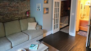 Ein Wohnzimmer mit Backsteinwand, einer Couch, einem Couchtisch mit einem Buch und einer Tür zum Badezimmer.