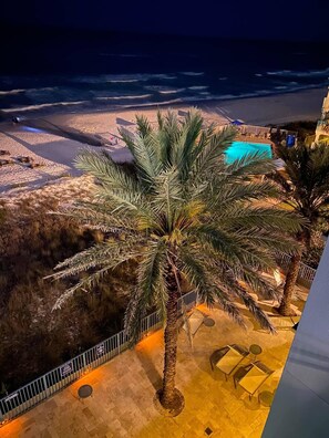 A rooftop terrace with a palm tree, a pool, and a view of the beach at night.