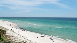 A beach with a pier extending into the ocean, sandy shores, and people enjoying the beach.
