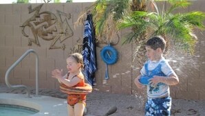 Deux enfants jouent près d’une piscine, avec un palmier et un mur couvert de graffitis.