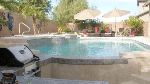 Une piscine équipée d’un barbecue intégré et de chaises longues.