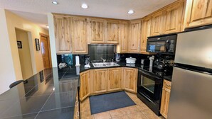 Eine moderne Küche mit Holzschränken, einem Edelstahlkühlschrank, einer Mikrowelle und einer schwarzen Arbeitsplatte.