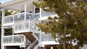 Une maison à plusieurs étages, avec une façade blanche, une terrasse en bois et un escalier.