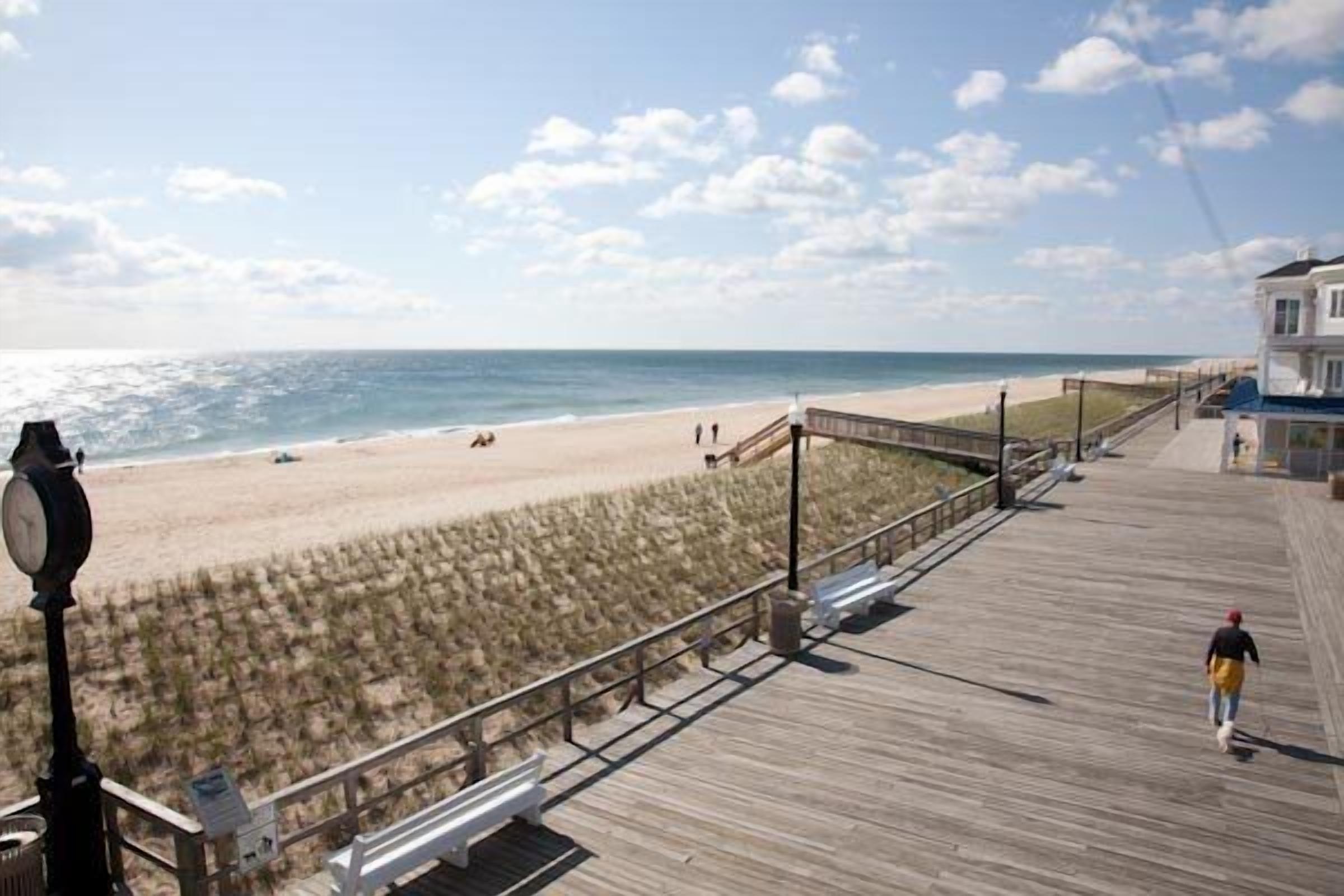 A beach boardwalk with a wooden walkway, benches, and a building with a blue roof.