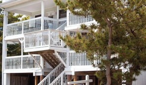 A multi-story house with a white exterior, a wooden deck, and a staircase.