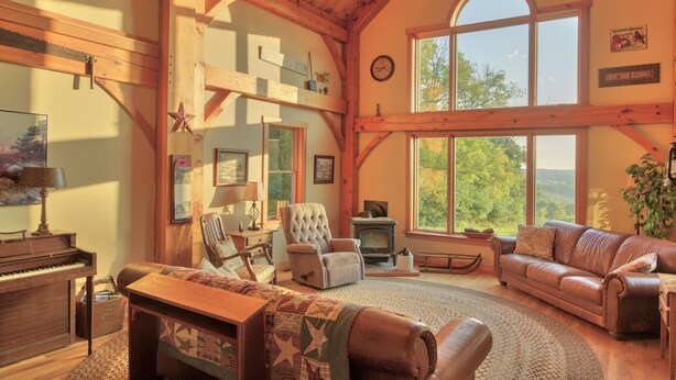 Un salón acogedor con un piano, sofás de cuero, una chimenea y grandes ventanales que ofrecen vistas al exterior.
